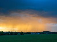 Regenschleier in Lichtkuppel unter dunkler Wolkenschicht am Abend